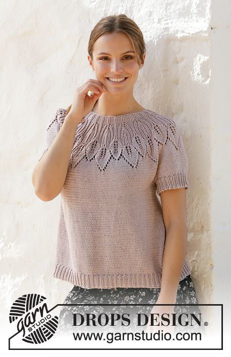 a woman standing next to a white wall wearing a sweater and smiling at the camera