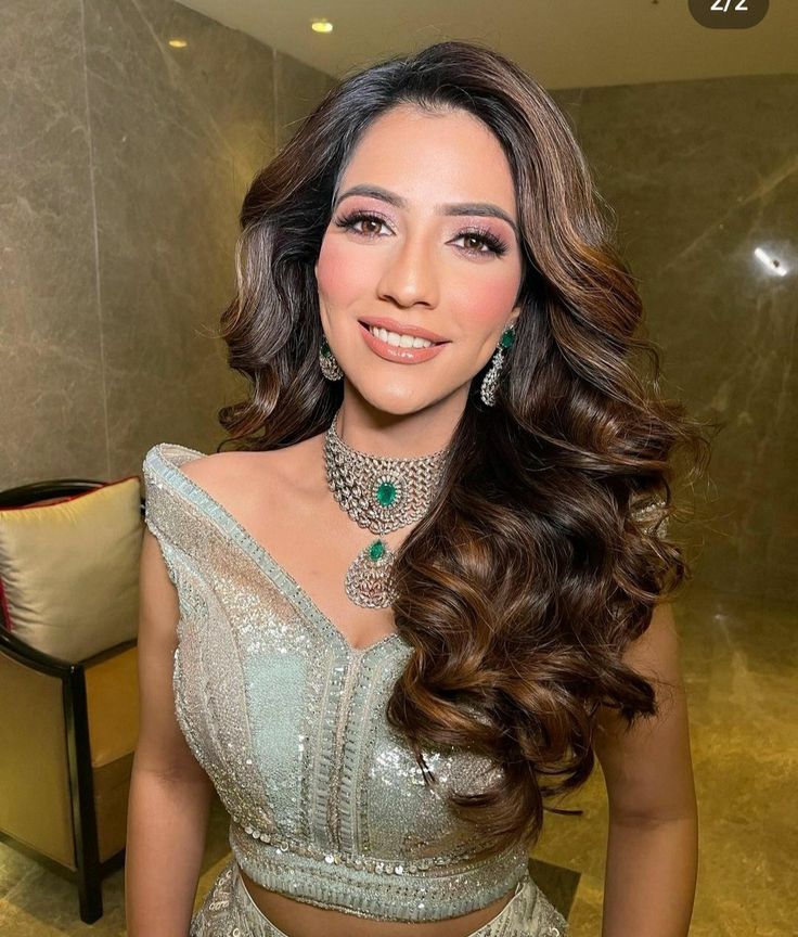 a woman with long hair wearing a silver dress and jewelry in front of a couch