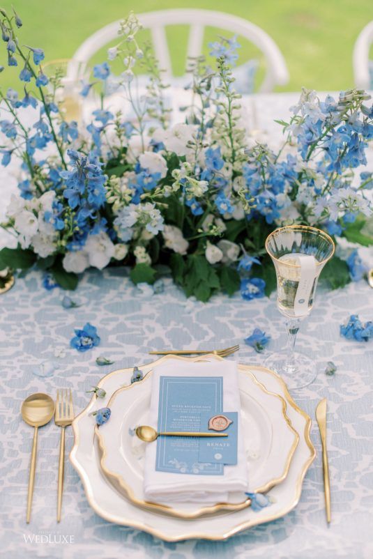 the table is set with blue and white flowers, silverware, and napkins