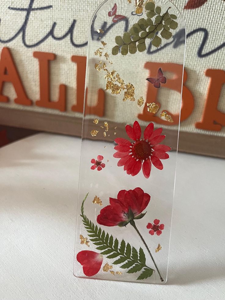 a clear vase with red flowers and green leaves on the bottom is sitting on a table