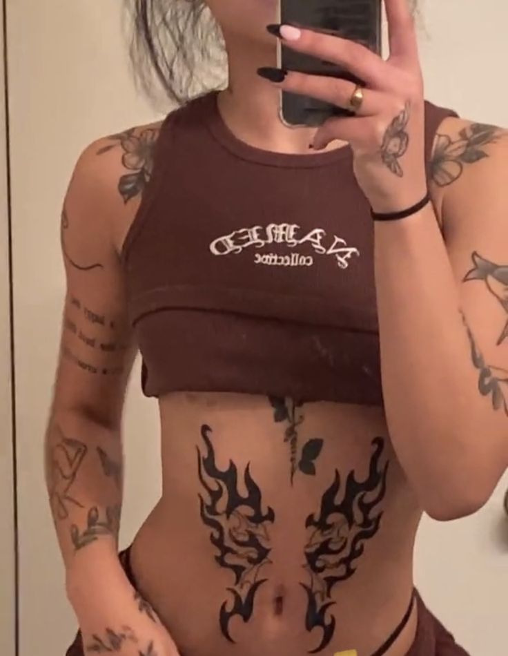 a woman with tattoos on her stomach holding a cell phone and taking a selfie