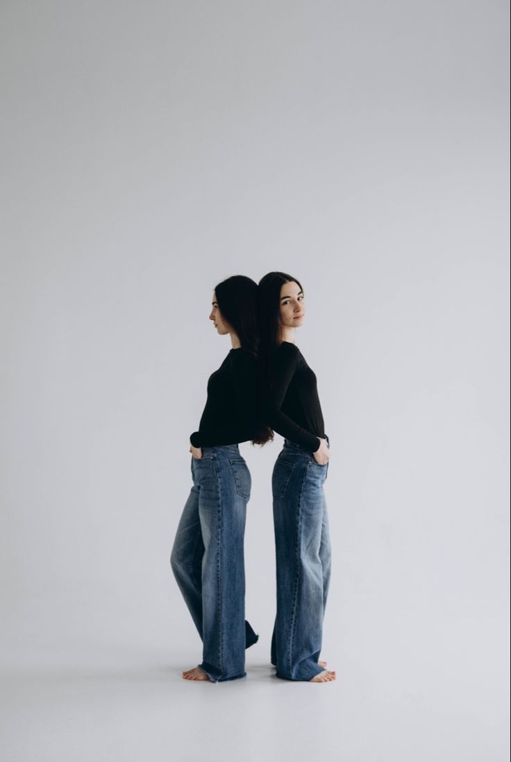 two women standing back to back in jeans