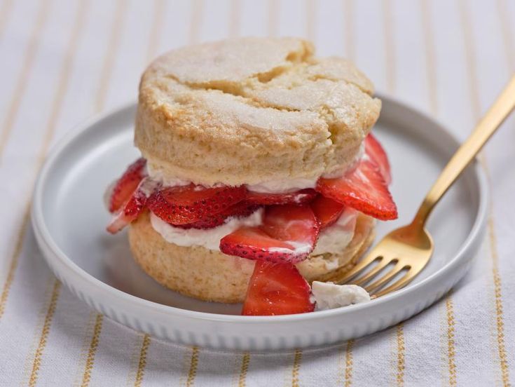 a white plate topped with two cookies covered in strawberries next to a golden fork