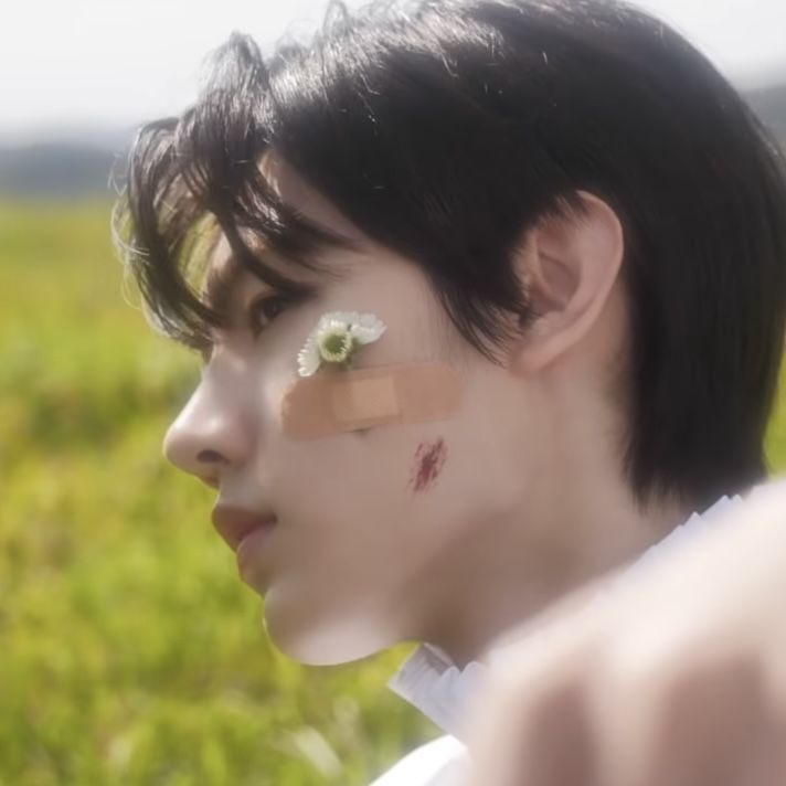 a man with black hair and flower on his forehead looking off into the distance while standing in a field