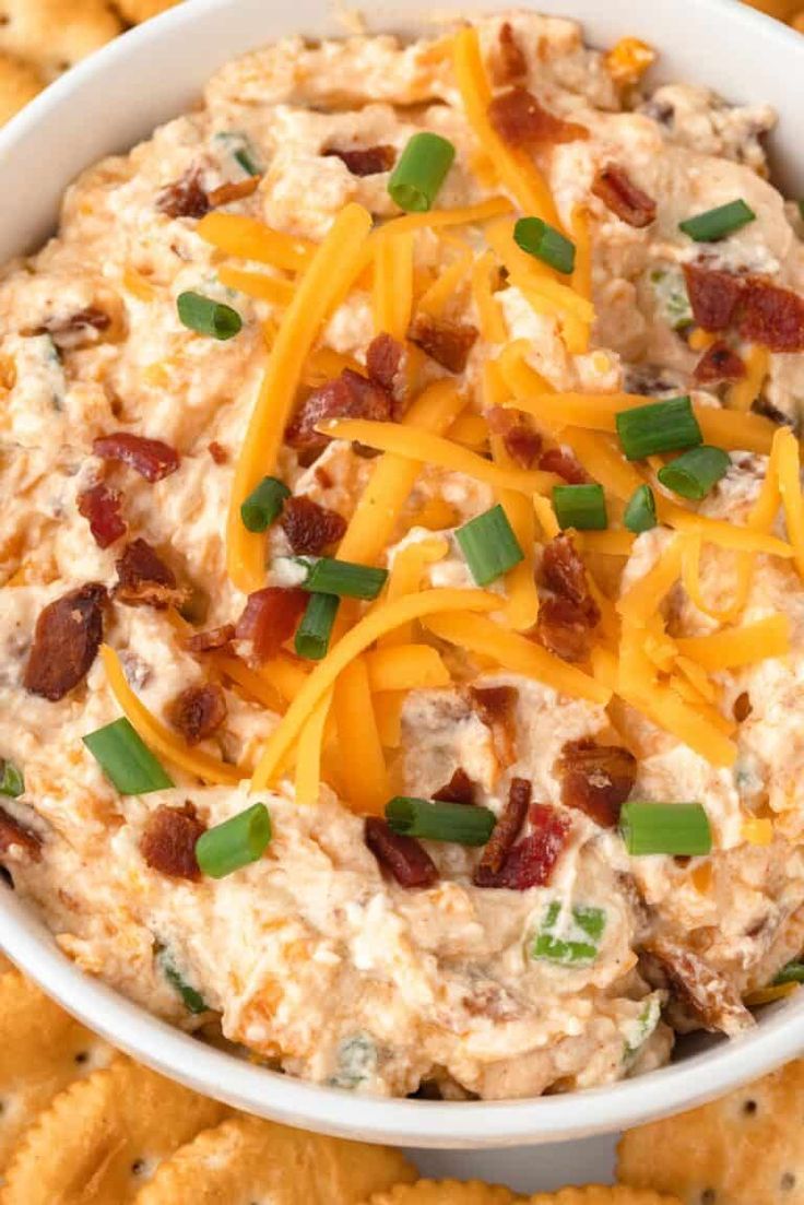 a white bowl filled with cheese and bacon dip surrounded by crackers