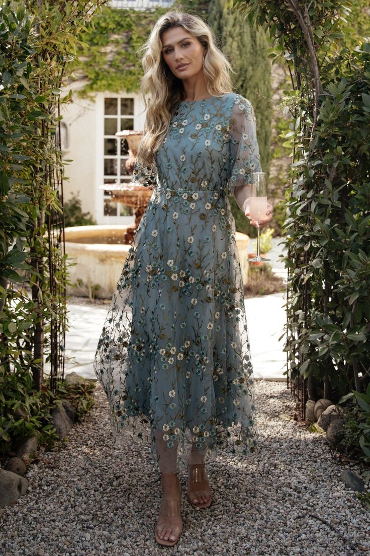 a woman standing in front of an archway wearing a blue dress with flowers on it