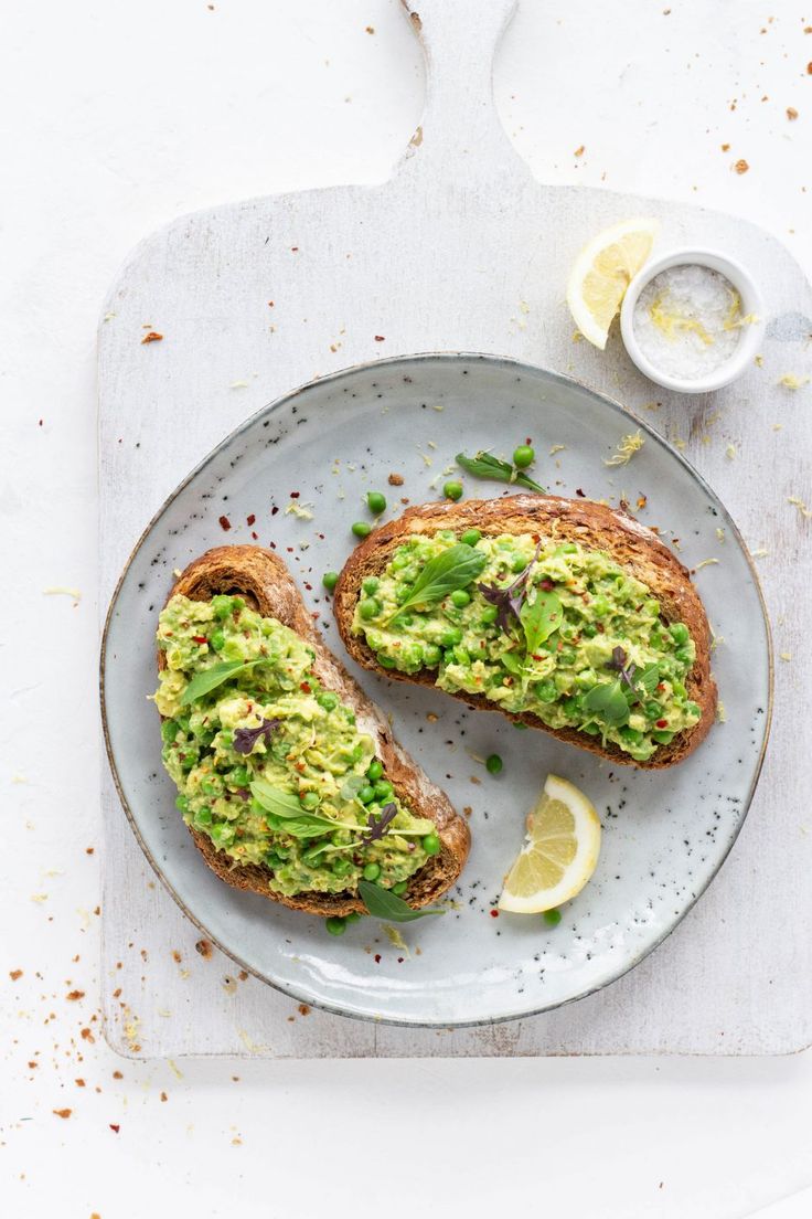 an avocado toast on a plate with lemon wedges