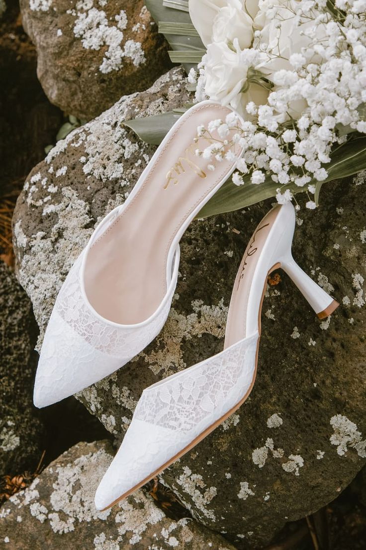 the bride's shoes are sitting on top of some rocks and white flowers in front of them