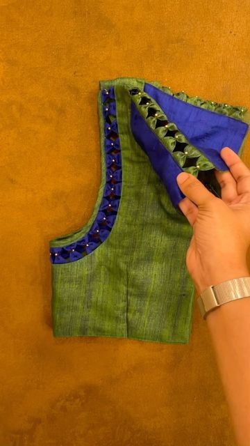 a woman is holding up a piece of fabric to sew on the back of a green and blue top