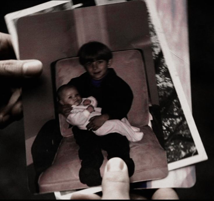 a person holding up a polaroid with a baby in it's lap and another hand holding the polaroid