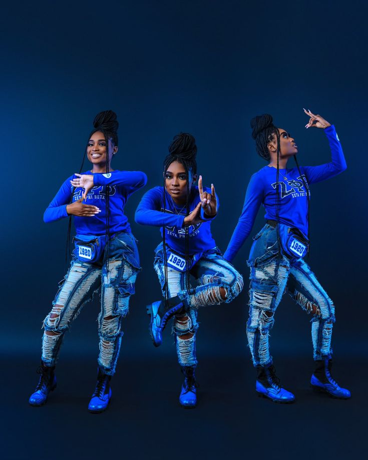 three young women in blue shirts and jeans posing for a photo with their hands up