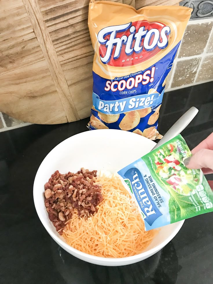 a person holding a bag of chips and some food in a bowl on the counter