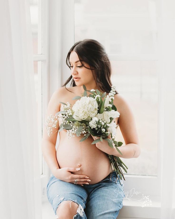 a pregnant woman sitting on a window sill with flowers in her belly and holding onto the side of her stomach