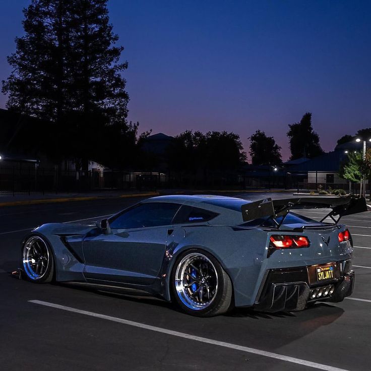 a gray sports car parked in a parking lot at night with its hood up and lights on