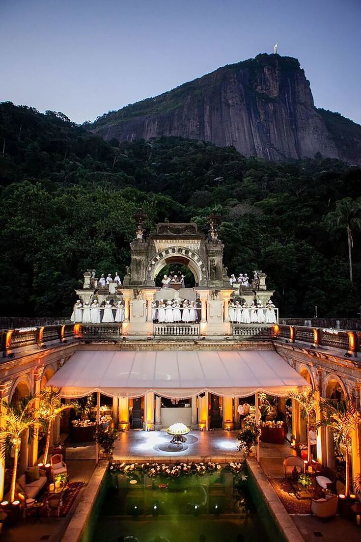 an aerial view of a building in the middle of a forest with mountains in the background