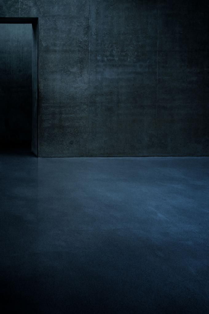 an empty room with dark walls and concrete flooring is lit by a single light