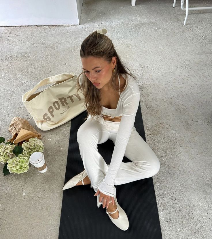 a woman is sitting on a yoga mat with her feet crossed and wearing white tights