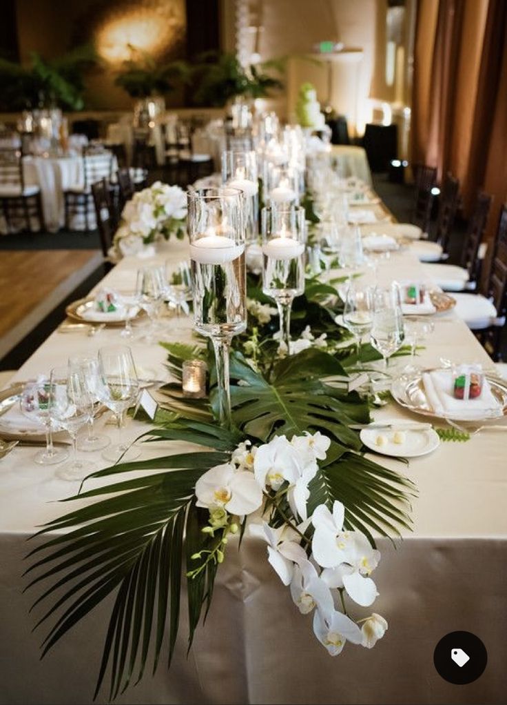 a long table with white flowers and greenery on it is set for a formal dinner