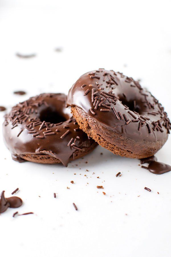 two chocolate doughnuts with sprinkles on them sitting on a white surface