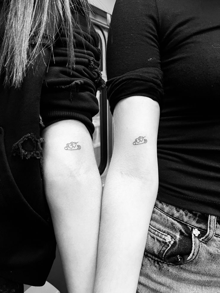 two women with matching tattoos on their arms, both holding each other's hands