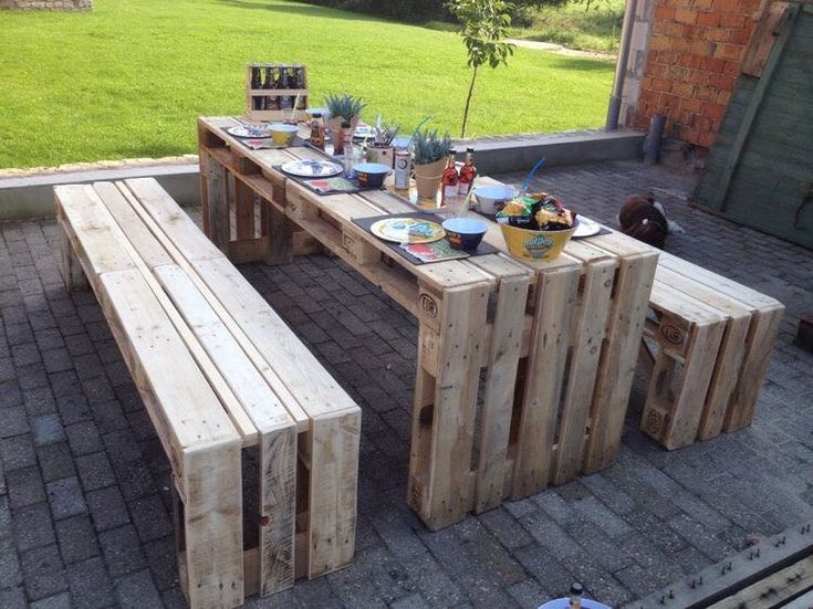 a picnic table made out of wooden pallets with plates and bowls on it, sitting in the middle of a brick patio