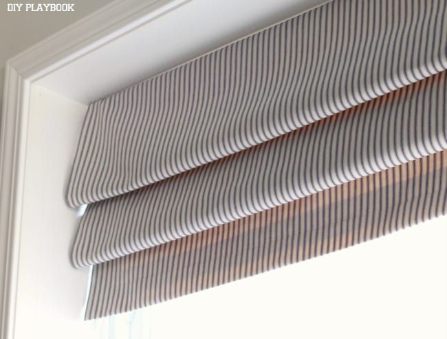 a close up view of a window with the blinds pulled back and striped fabric on it