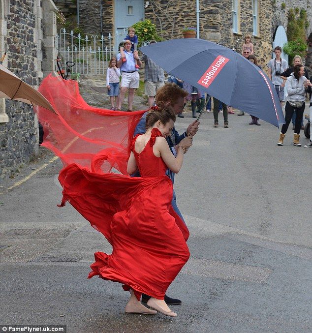 a woman in a red dress is holding an umbrella and walking down the street while people watch