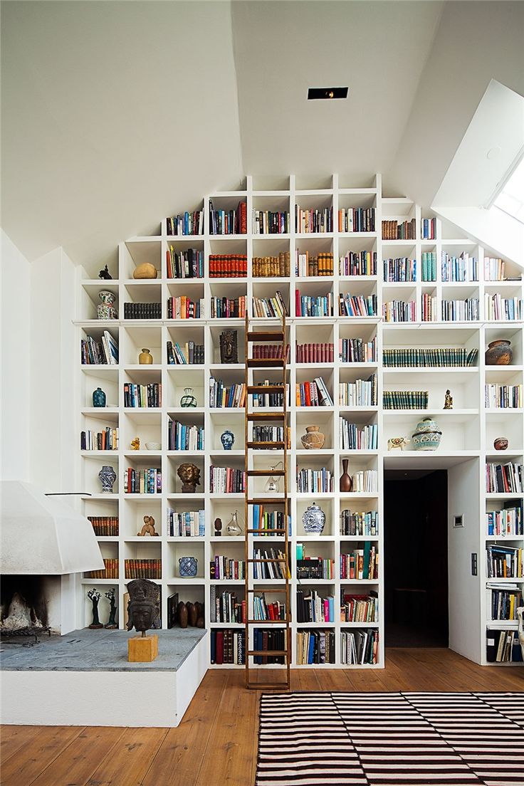 a living room filled with lots of books on top of a white book shelf next to a fireplace