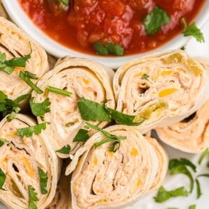 several burritos on a plate with salsa in the bowl and sauce behind them