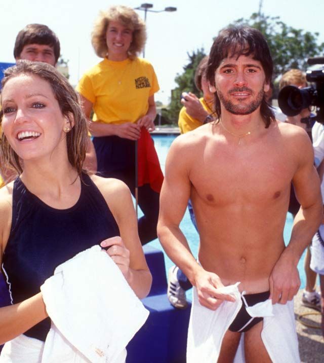 two young people standing next to each other in front of a swimming pool with towels around them