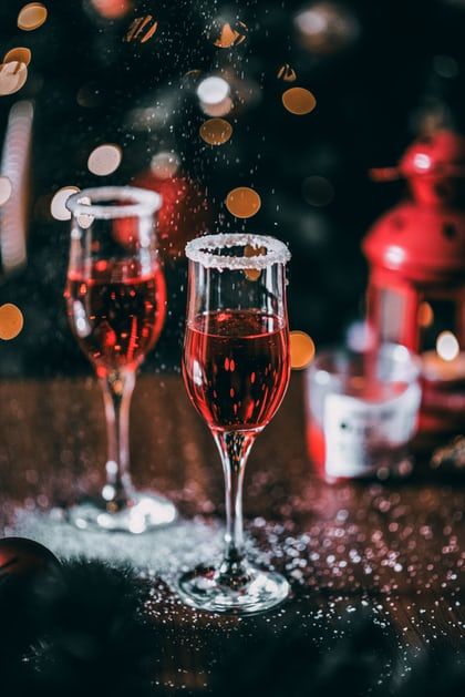 two glasses of wine sitting on top of a table next to bottles and cans with lights in the background