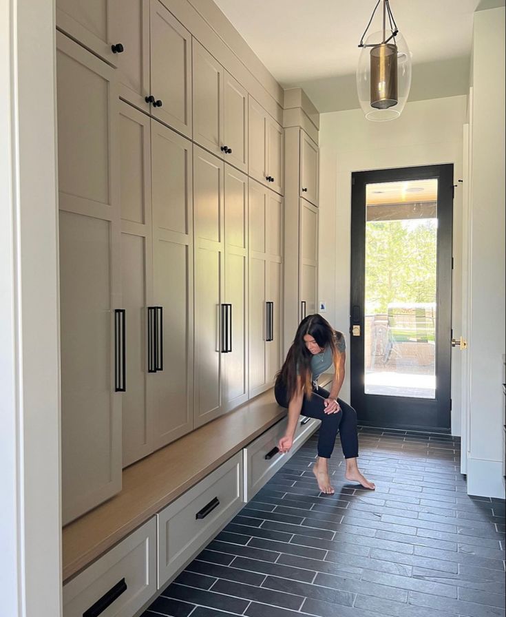 a woman sitting on a bench in a kitchen next to some cupboards and doors