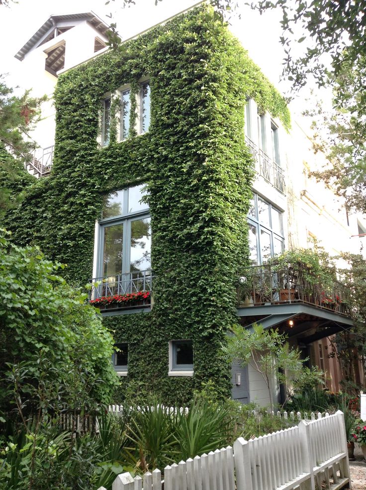 a building covered in vines and flowers next to a white fence