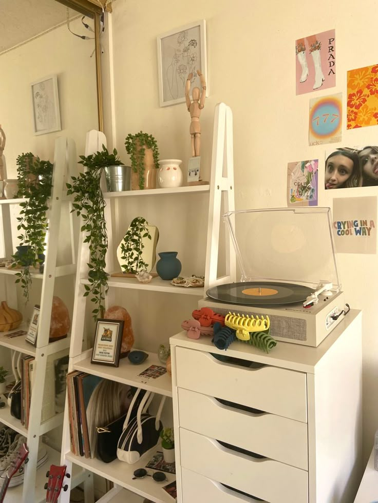 a record player sitting on top of a white dresser next to a shelf filled with plants