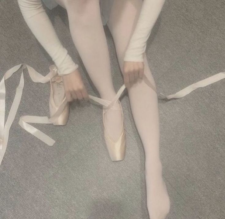 a ballerina tying her ballet shoes on the floor with white ribbons around her ankles