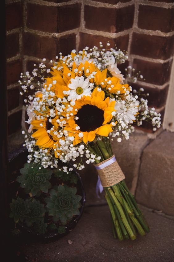 a bouquet of sunflowers and baby's breath sits in front of a brick wall