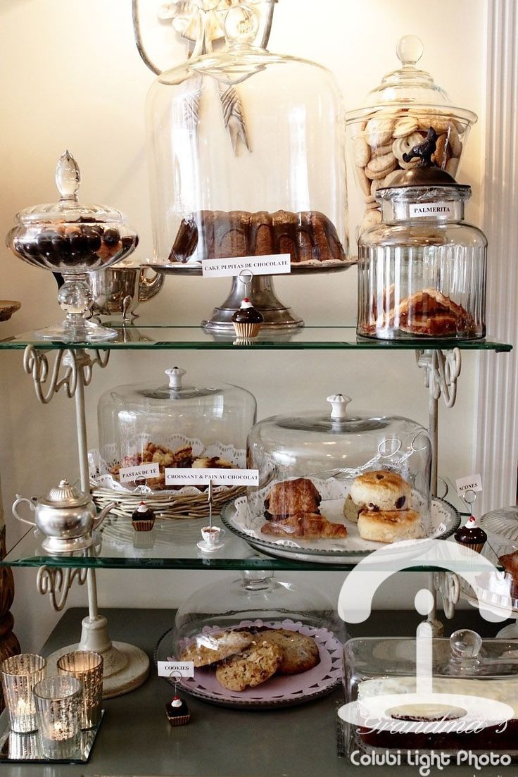 a display case filled with lots of pastries and desserts on glass shelves in front of a chandelier