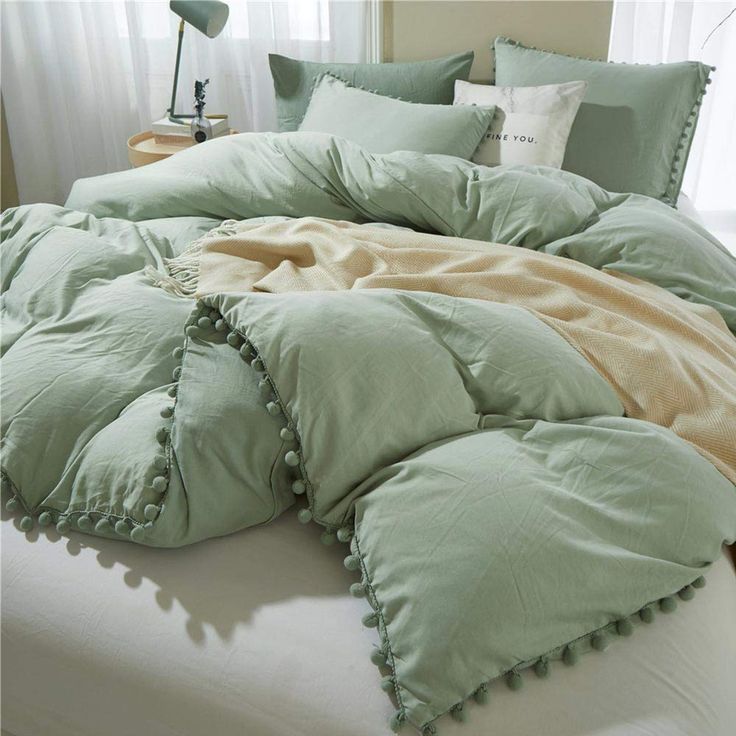 an unmade bed with green and beige comforters on it in a bedroom setting