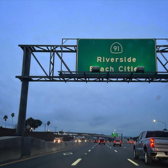 an interstate exit sign above a highway with cars driving on the road below it at dusk