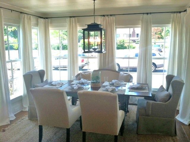 a dinning room table and chairs in front of large windows with white drapes