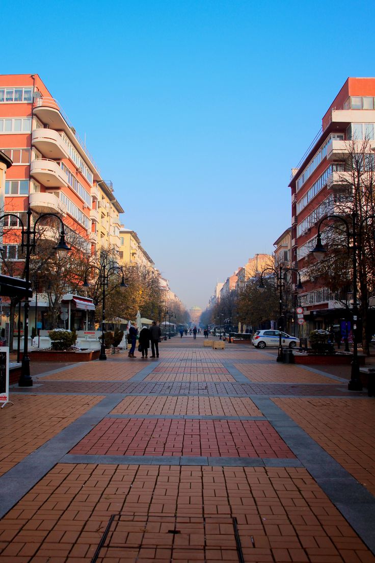 an empty city street with people walking on the sidewalk and cars parked in the distance