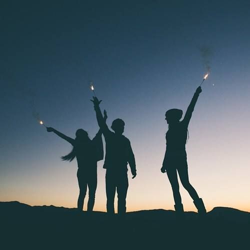 three people standing on top of a hill with their arms in the air while holding sparklers