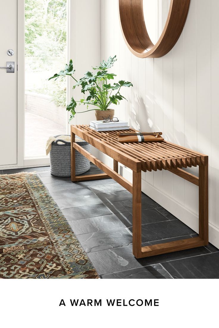 a wooden bench sitting in front of a door next to a rug and potted plant