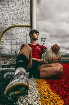 a man sitting on the ground with a soccer ball in front of him and his legs crossed