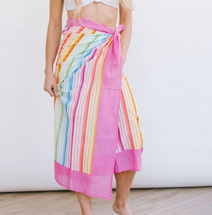 a woman standing in front of a white wall wearing a pink skirt with multicolored stripes