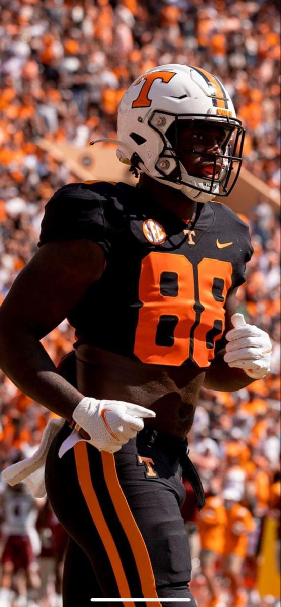 a football player is running with the ball in his hand and an orange and white uniform on