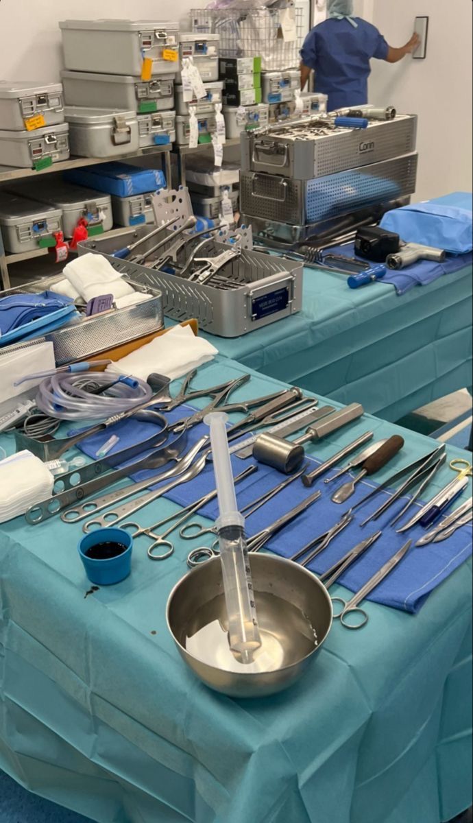 surgical instruments are set up on tables in an operating room, with medical equipment scattered about the table