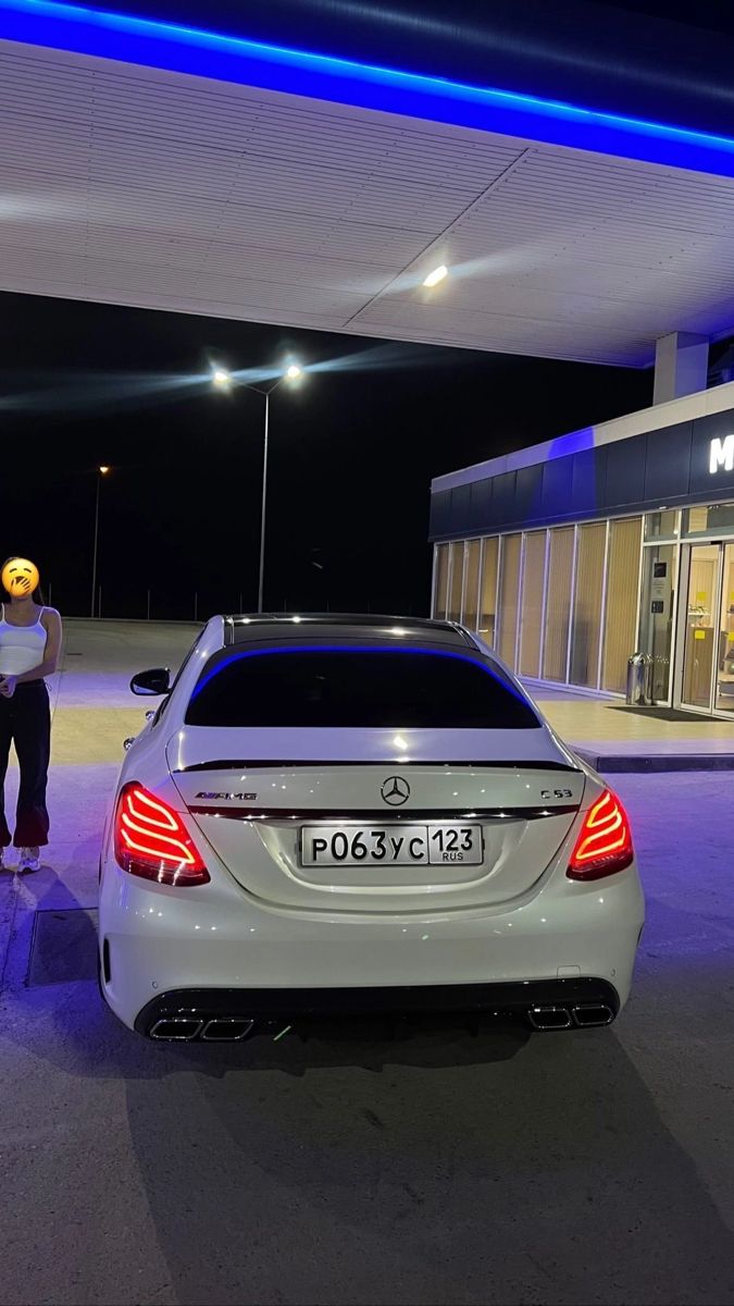 a man standing next to a white car in front of a gas station at night