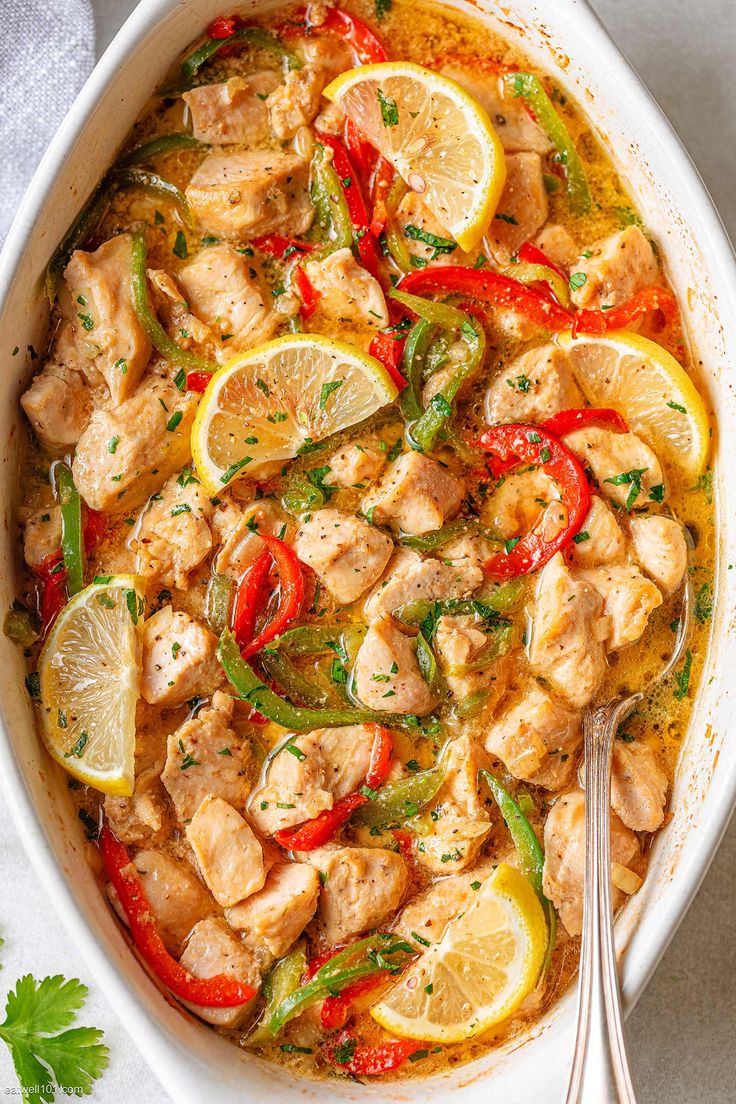 a pan filled with chicken, peppers and lemons on top of a white table