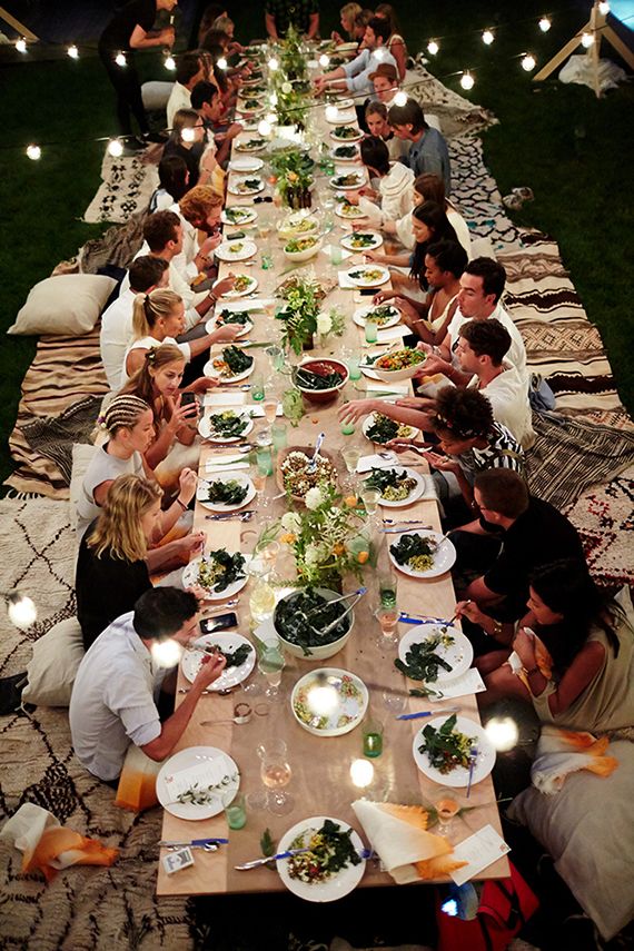 a group of people sitting at a long table with plates and bowls of food on it